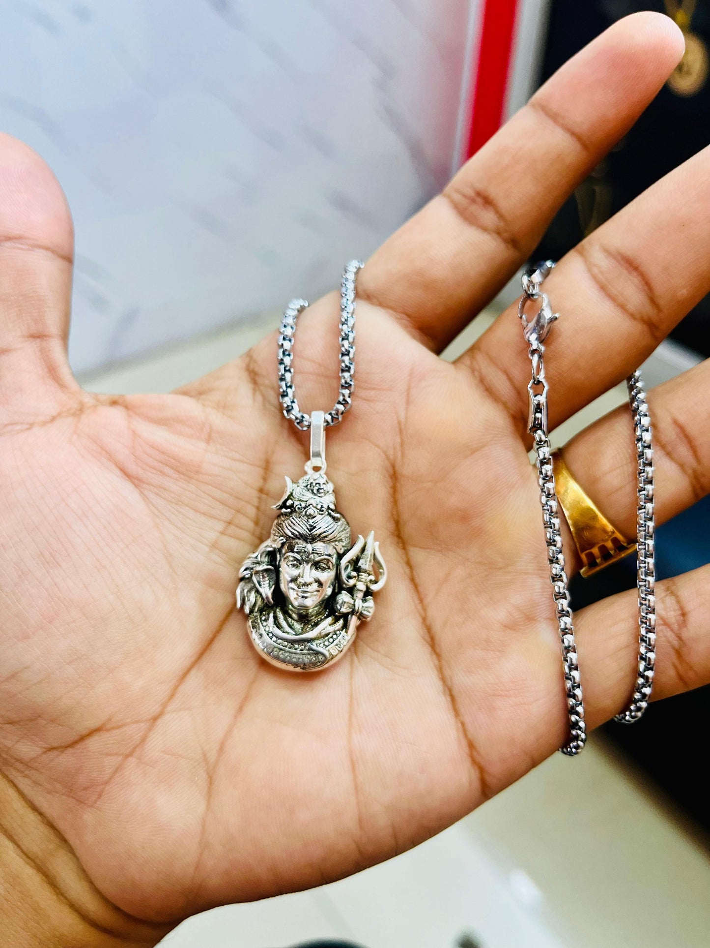 Silver Mahadev pendant necklace with intricate design shown in a hand