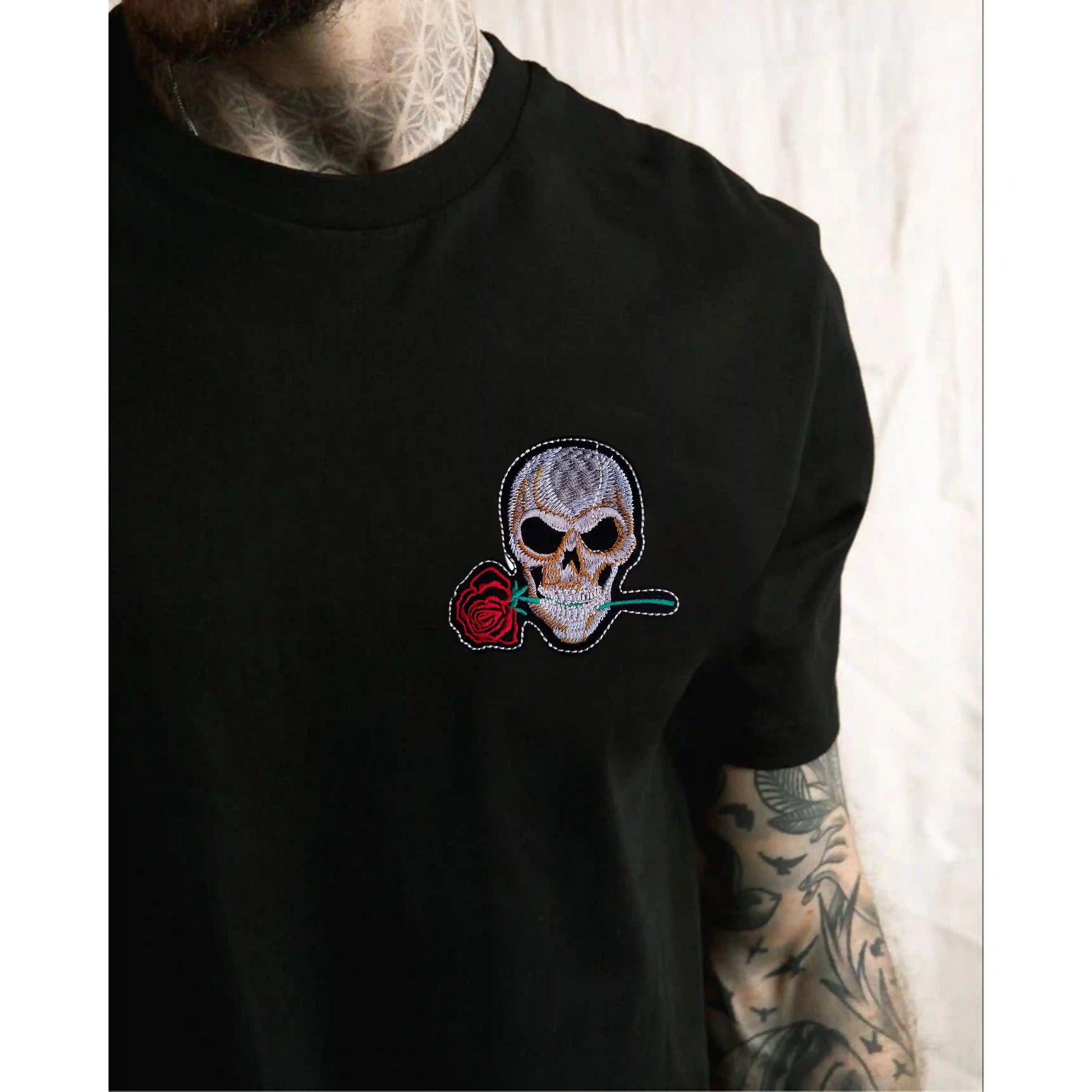 Black t-shirt with a skull and rose patch worn by a person with tattoos.