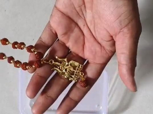 Trishul spiritual charm on a decorative necklace held in a hand, featuring intricate bead details